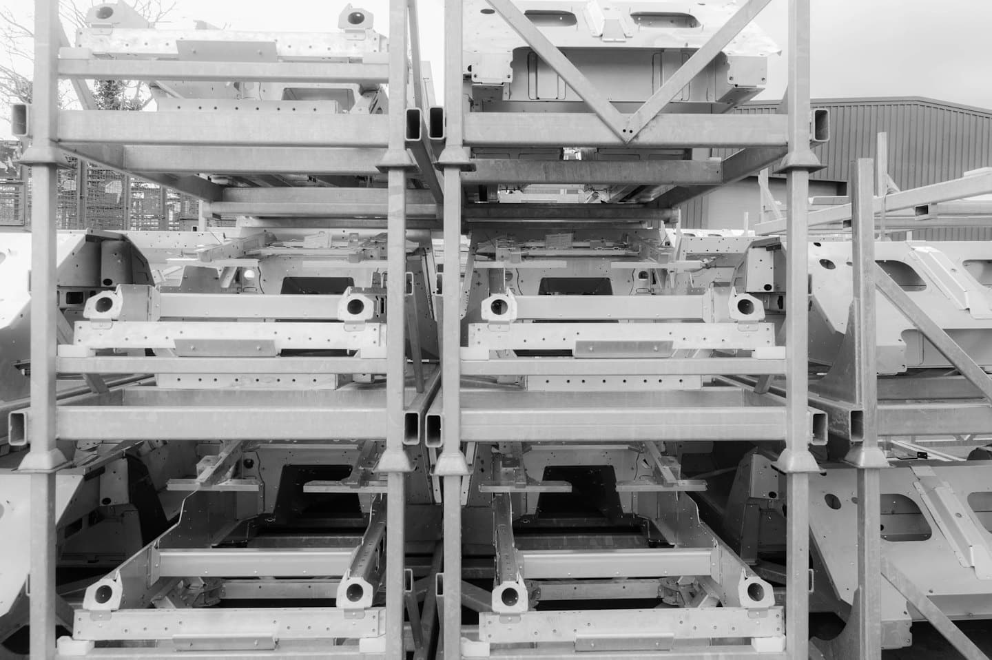 Metal car chassis stacked on industrial shelving outdoors.
